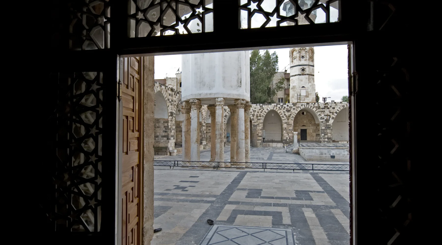 The courtyard of the Great Mosque of Hama seen through a carved doorway, its treasury dome standing on ancient columns