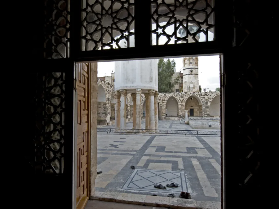 The courtyard of the Great Mosque of Hama seen through a carved doorway, its treasury dome standing on ancient columns