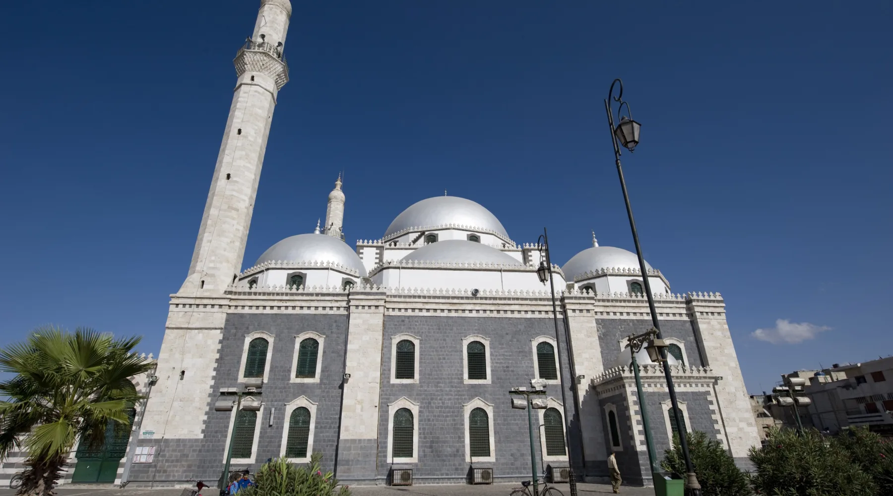 The banded stone facade, silver domes and tall minaret of the mosque of Khalid ibn al-Walid in Homs