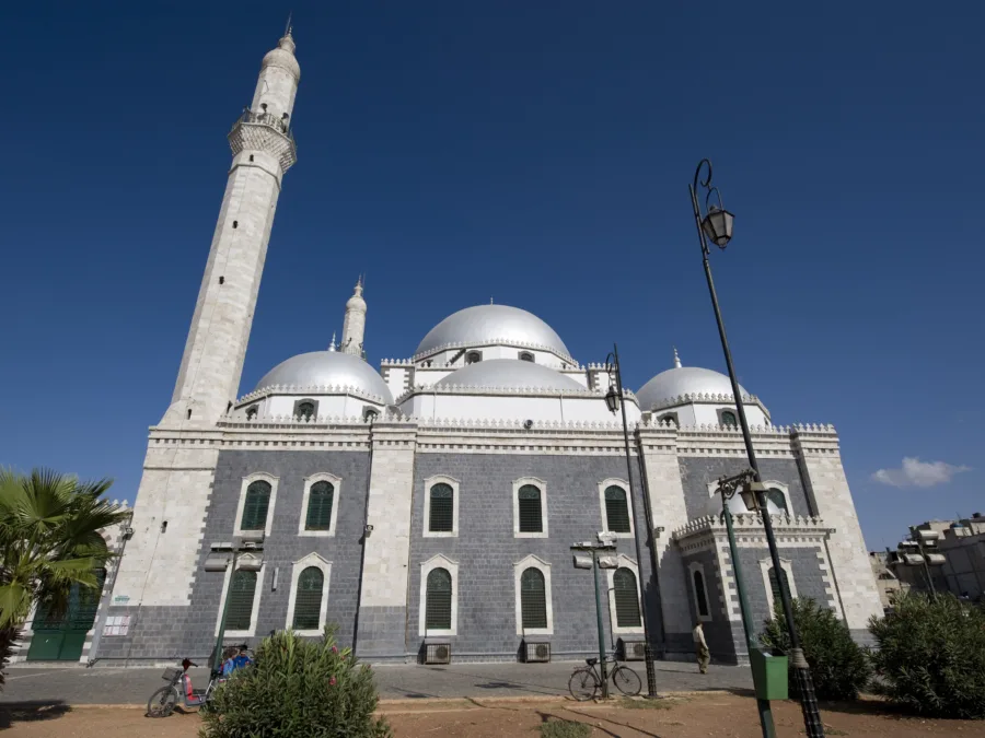 The banded stone facade, silver domes and tall minaret of the mosque of Khalid ibn al-Walid in Homs