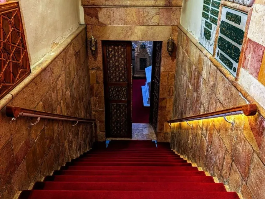Red carpeted stairs leading down to the doorway of the tomb chamber of Ibn Arabi in Damascus, an Ottoman tughra carved on the marble above it