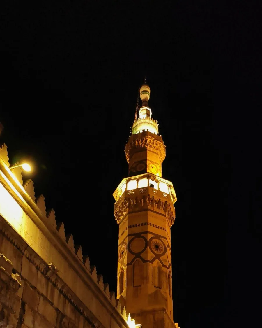 The Minaret of Isa at the Umayyad Mosque lit against the night sky above the old city wall