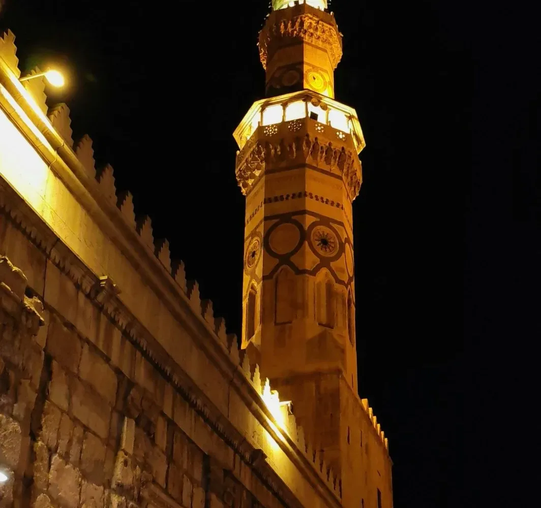The Minaret of Isa at the Umayyad Mosque lit against the night sky above the old city wall