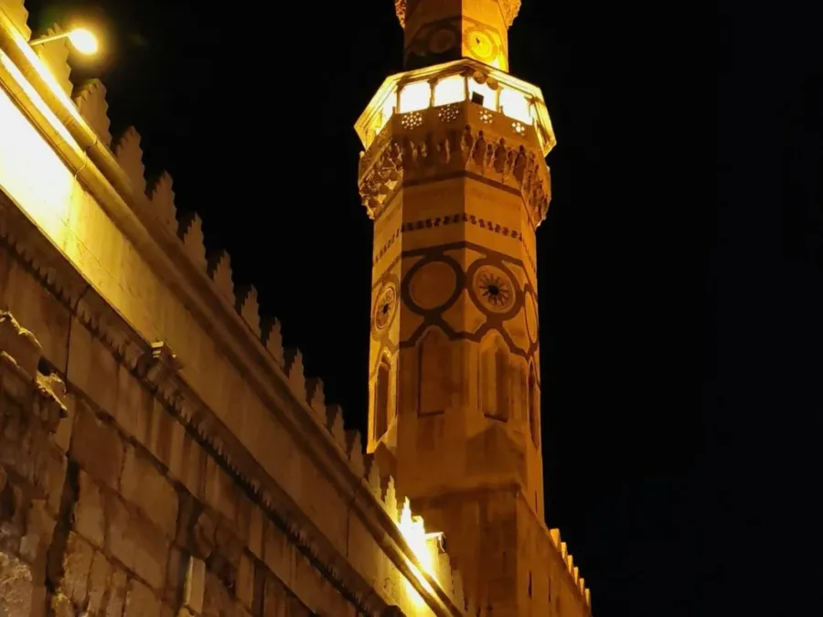 The Minaret of Isa at the Umayyad Mosque lit against the night sky above the old city wall
