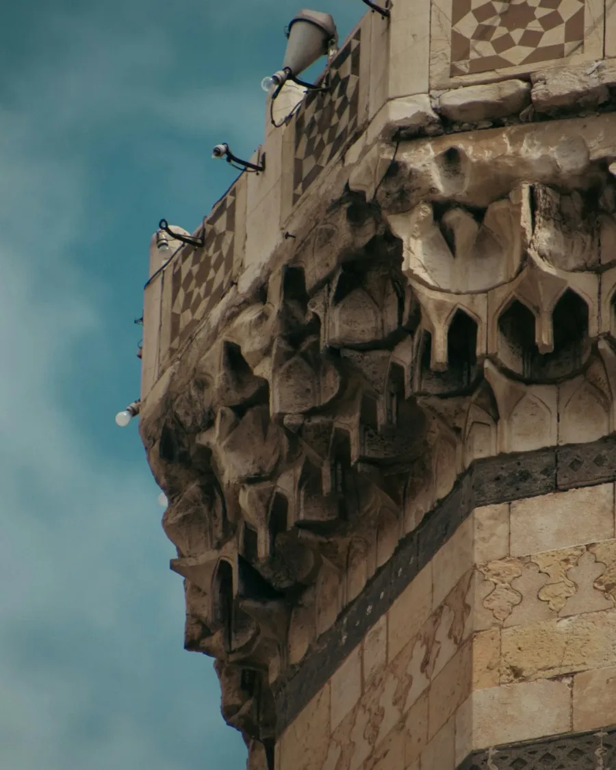 Carved muqarnas corbelling and ablaq stone banding on the balcony of a Damascene minaret against a blue sky