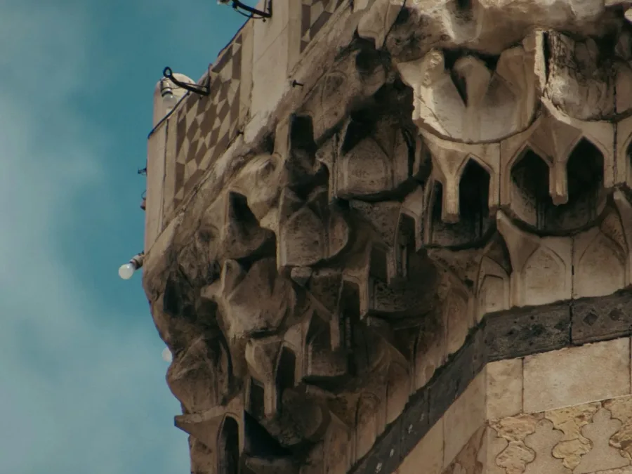 Carved muqarnas corbelling and ablaq stone banding on the balcony of a Damascene minaret against a blue sky
