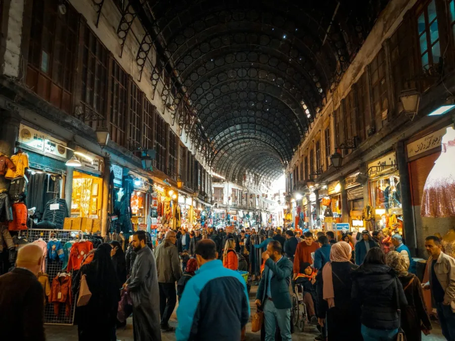 Crowds walking beneath the vaulted iron roof of Souk al-Hamidiyah, lit shopfronts on both sides