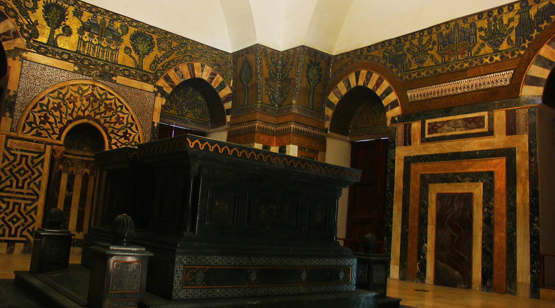 The dark marble cenotaph of Sultan Baybars beneath a band of gold mosaic in the Zahiriyya madrasa, Damascus